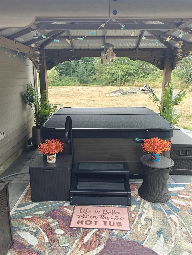 Covered hot tub under a backyard gazebo with a welcome mat