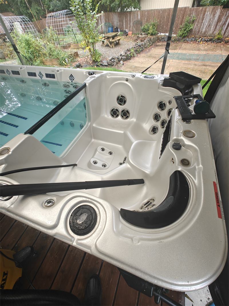 Swim spa with clear water on a covered deck beside a backyard garden