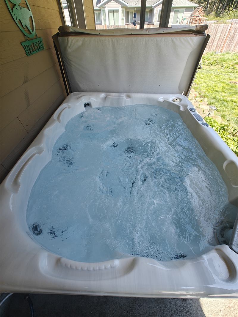 Hot tub with clear bubbling water on a covered patio next to a backyard lawn