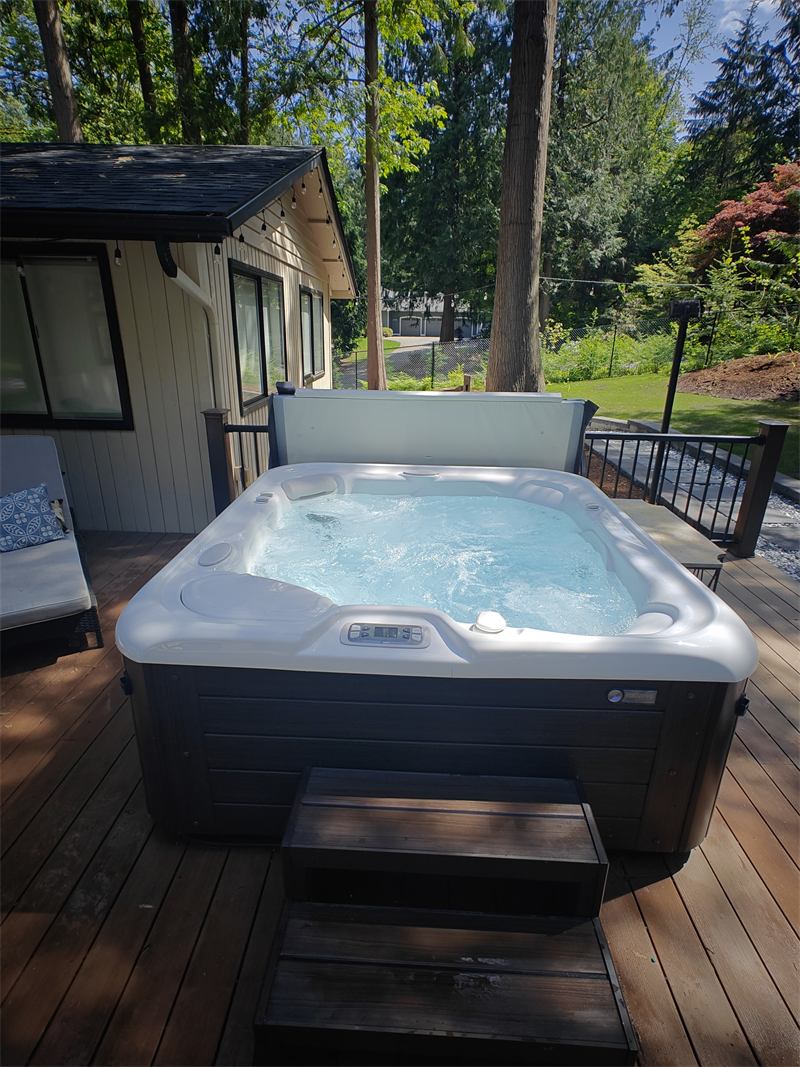 Backyard hot tub with clear bubbling water on a sunlit wood deck strung with lights